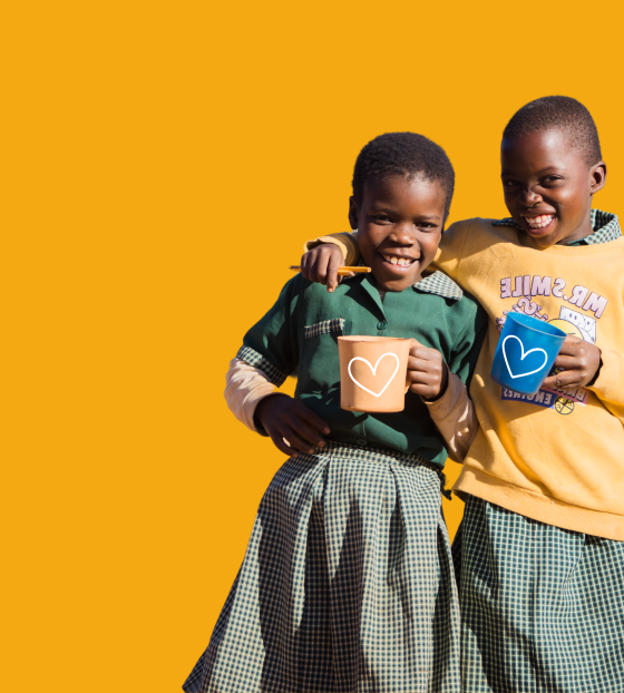 Niño sonriendo en su escuela después de recibir una comida de Mary’s Meals, representando el impacto de donar mensualmente. Campaña Hazte Socio - Alimenta su esperanza.