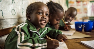 Un niño joven toma apuntes en clase en Kenia.