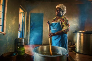 Una cocinera voluntaria se ríe mientras revuelve una olla de comida en Malawi.